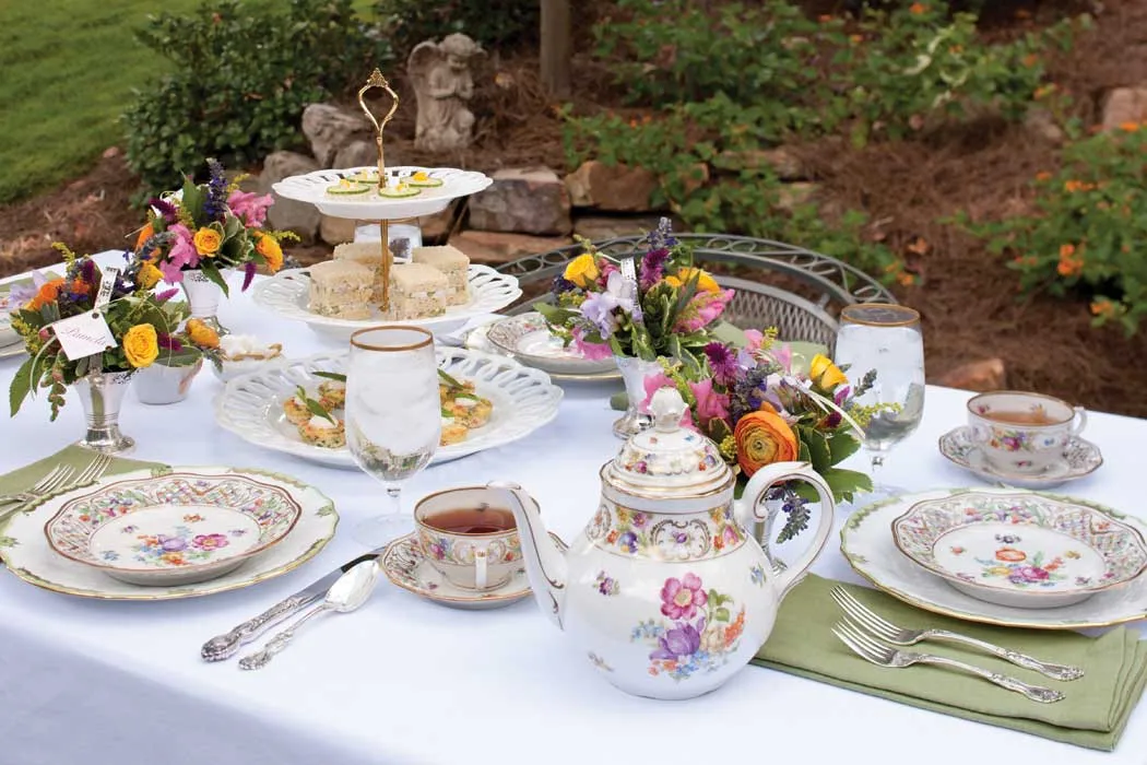 An elegant outdoor garden high tea table setting with teapots and fresh florals