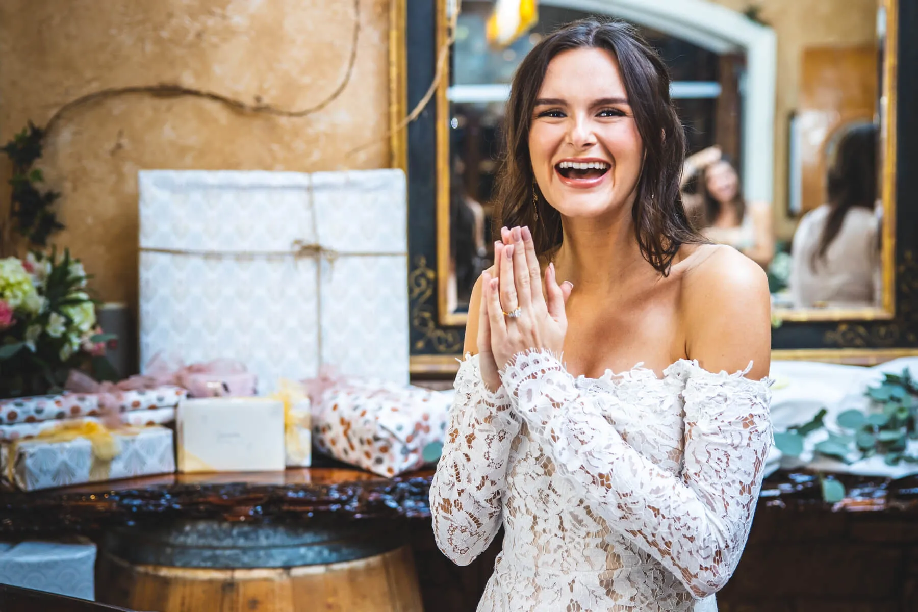 A bride laughing while opening gifts surrounded by guests at a kitchen tea