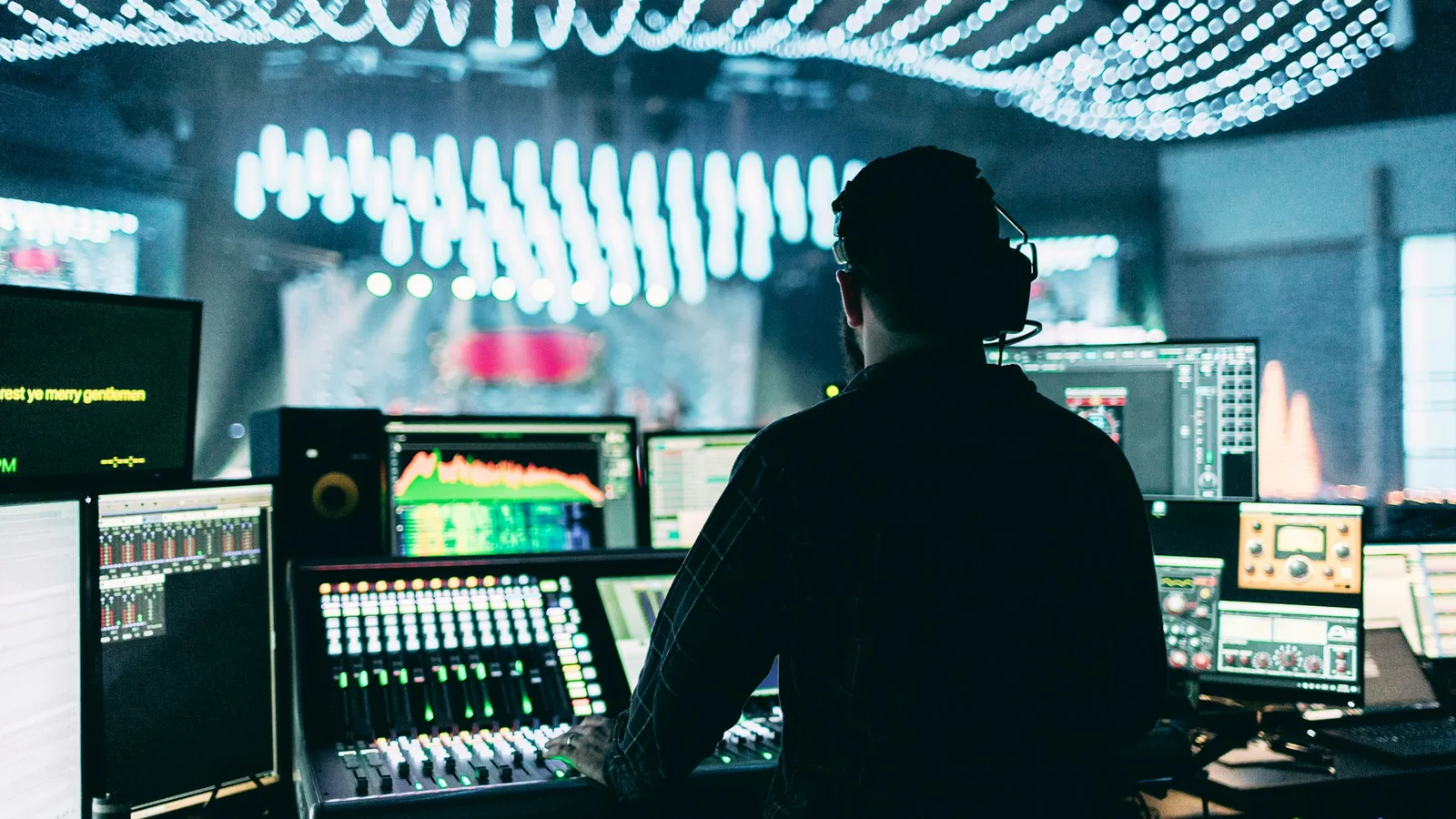 An audio technician wearing headphones at an illuminated event mixing desk