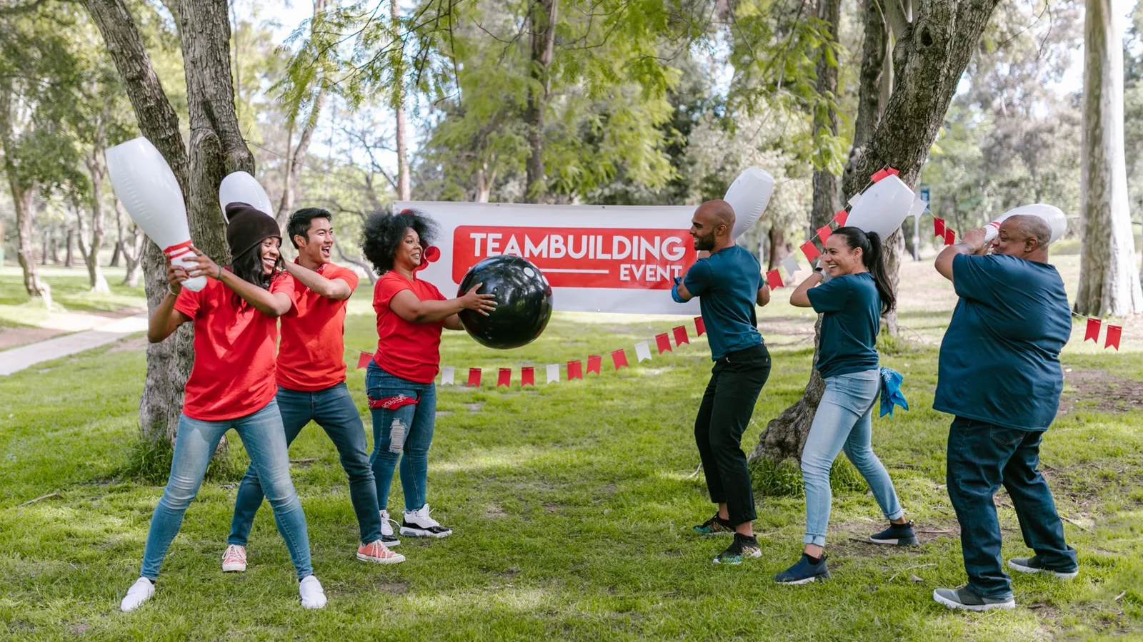 Adults in team shirts playing an outdoor team-building game on a grassy field under trees