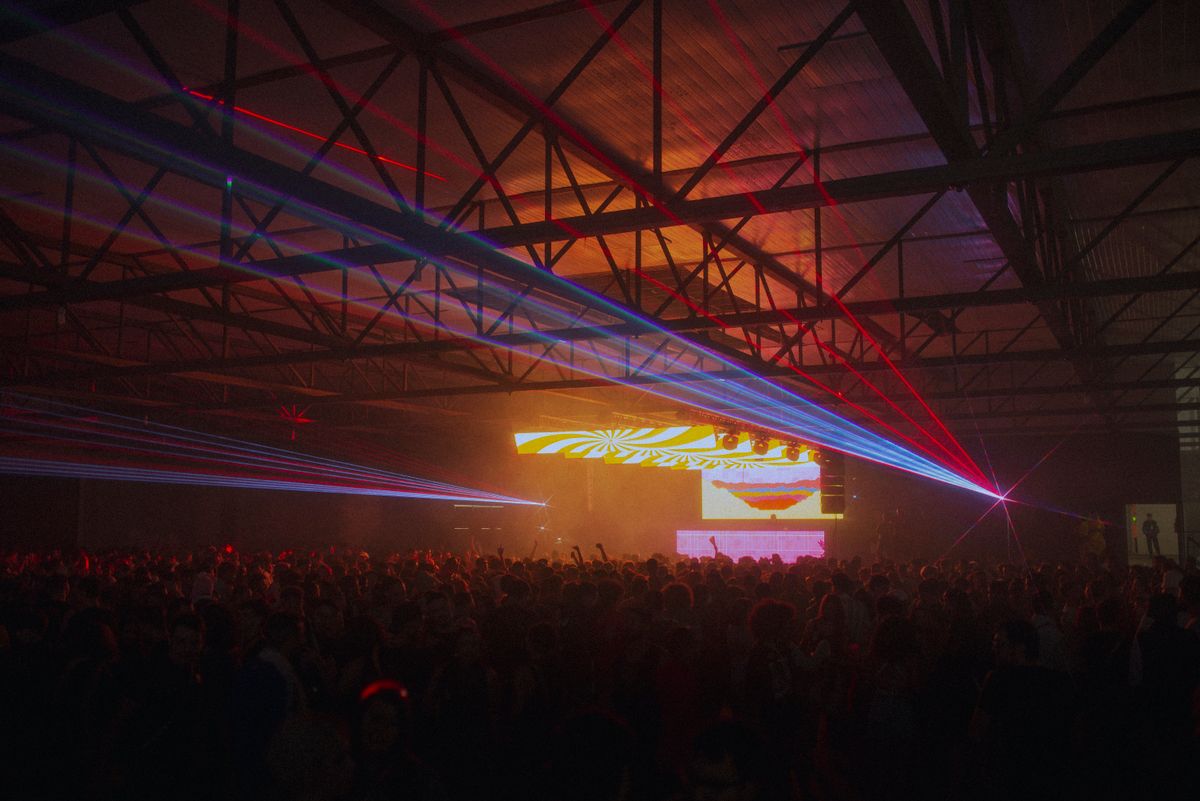 Secret Warehouse Rave theme: laser beams cutting through haze over a crowd